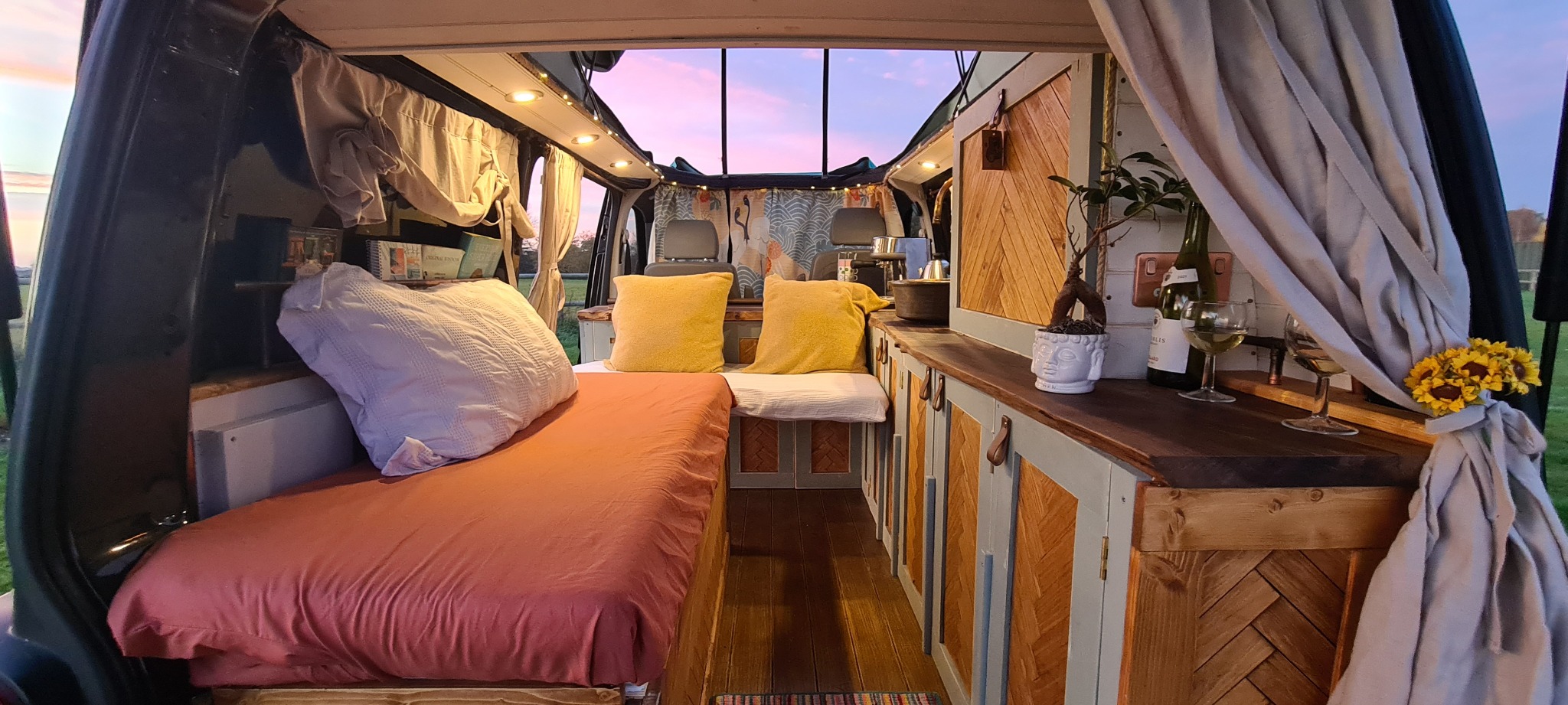 Warm handmade campervan interior with bed, cabinetry and timber worktops at sunset